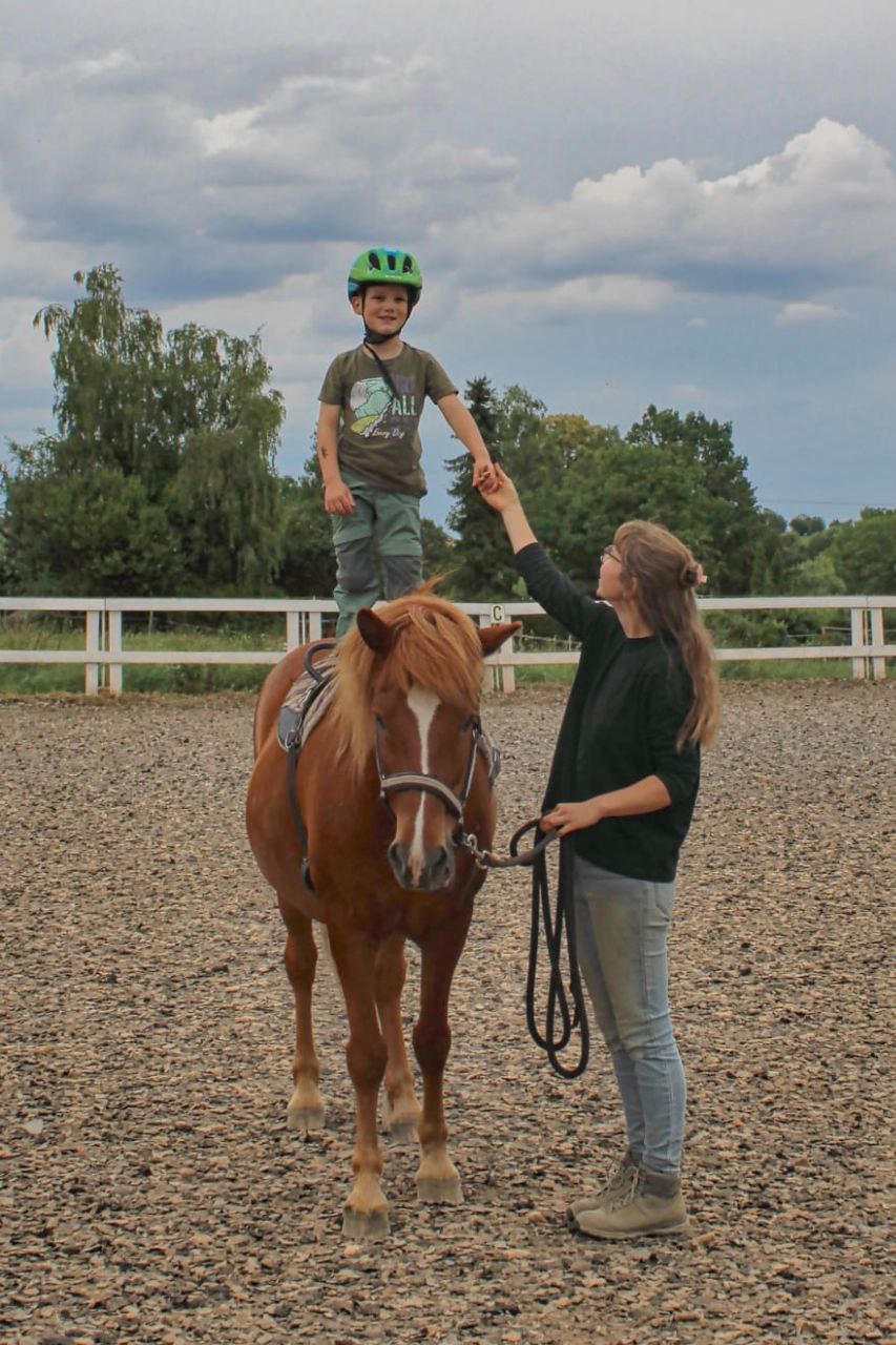 Kind steht auf Pony, Trainerin sichert